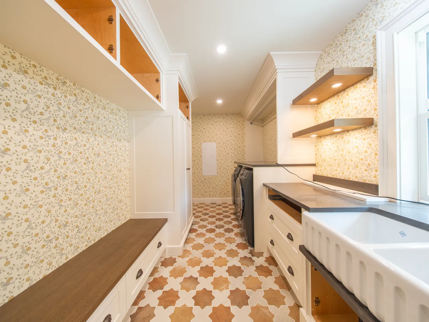Laundry room with patterned wallpaper, floating shelves, and farmhouse sink