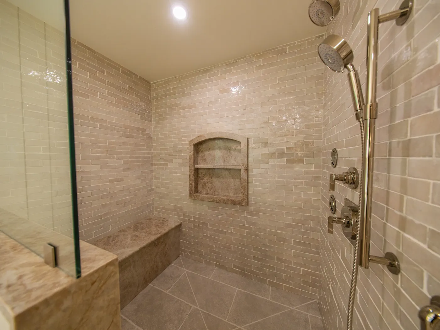 Walk-in shower with marble-look tile, bench, and niche