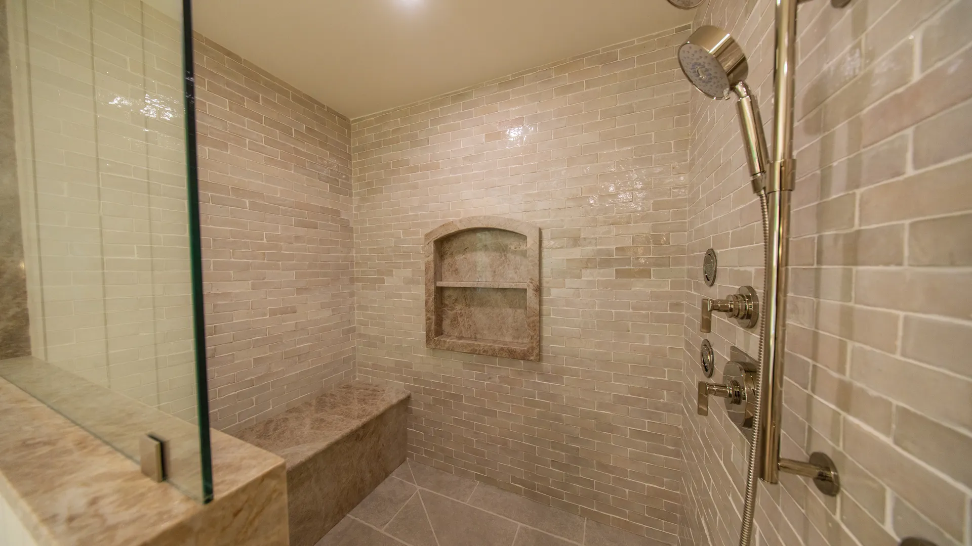 Walk-in shower with marble-look tile, bench, and niche