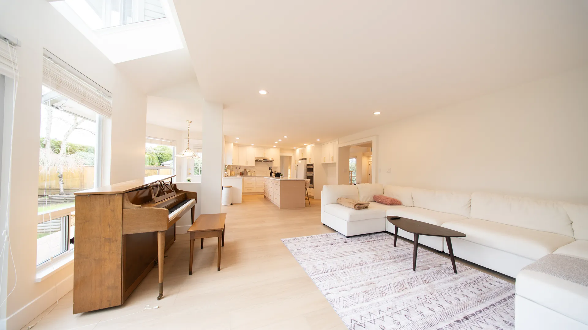 Living room with vaulted ceiling, skylights, and piano